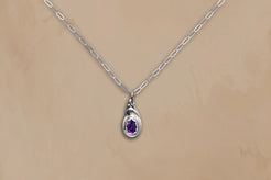Silver necklace with a teardrop-shaped pendant featuring a purple gemstone on a beige background