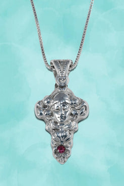 Silver pendant with face design and red gemstone on a light blue background