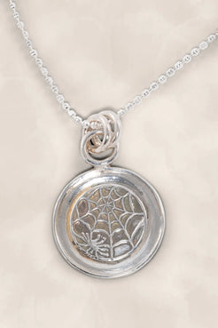 Silver pendant with spider web design on a beige background