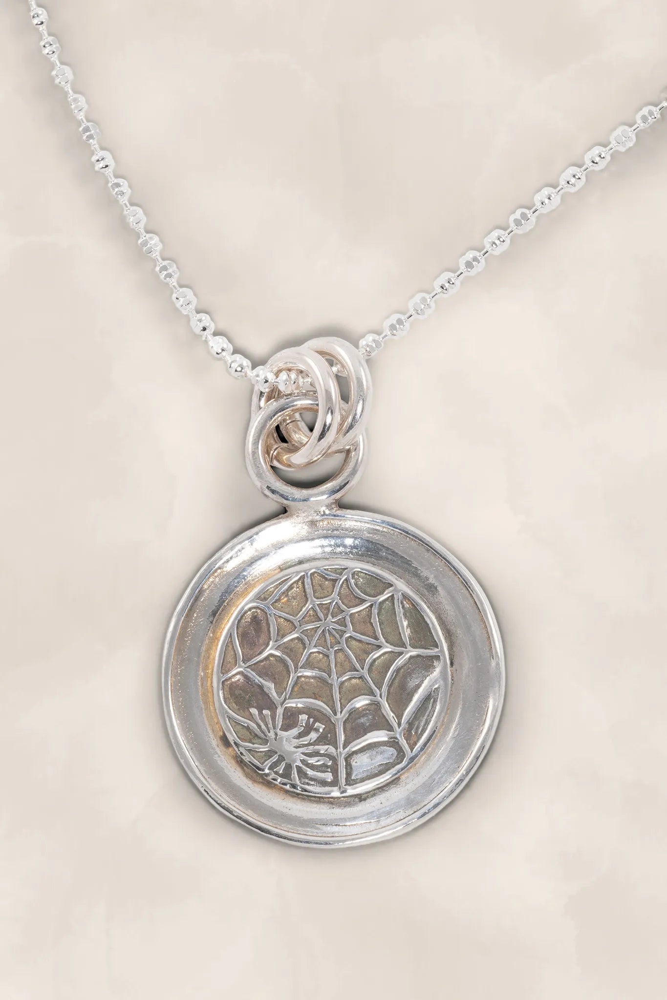 Silver pendant with spider web design on a beige background