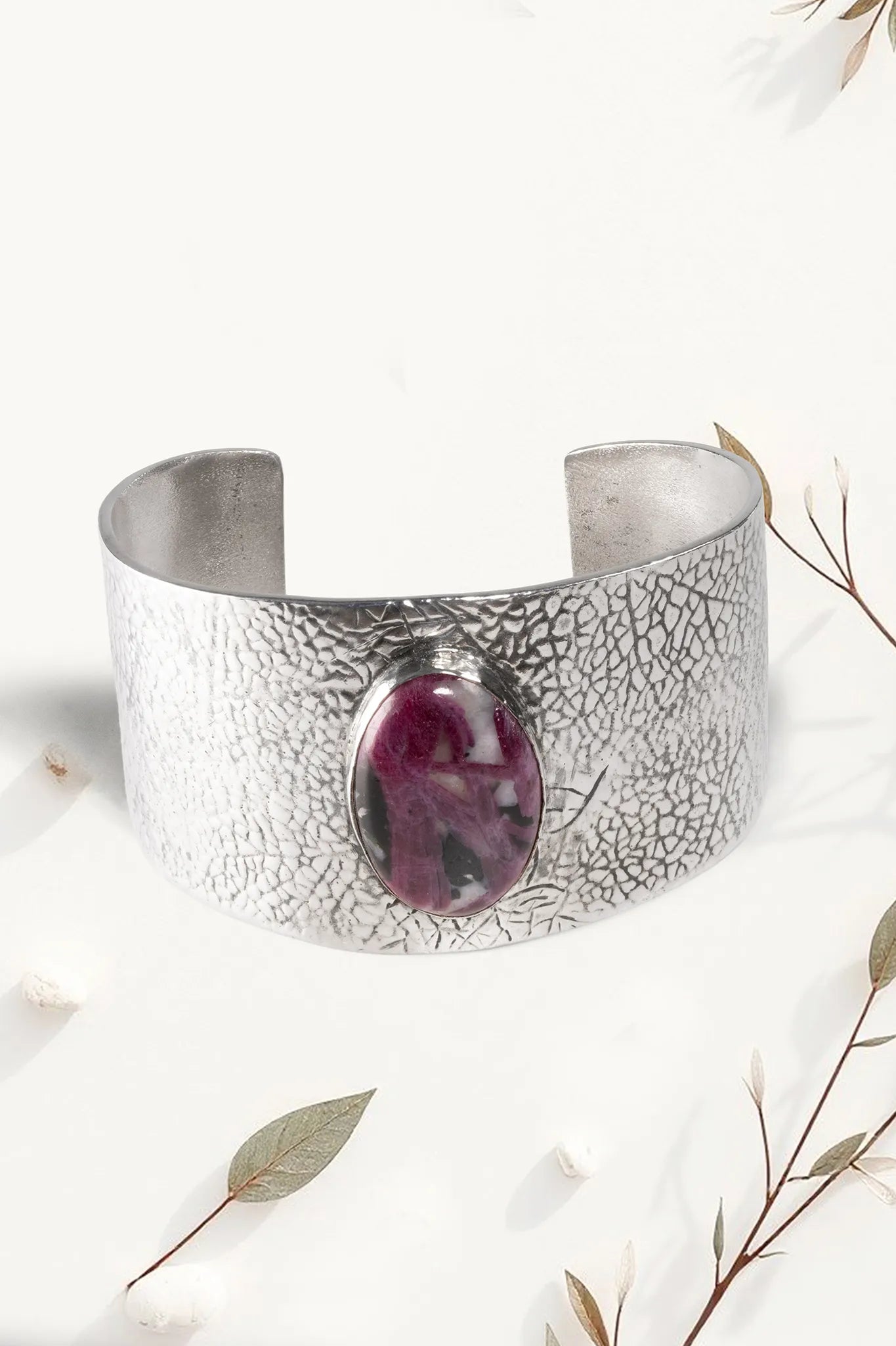 Silver cuff bracelet with a purple stone on a white background