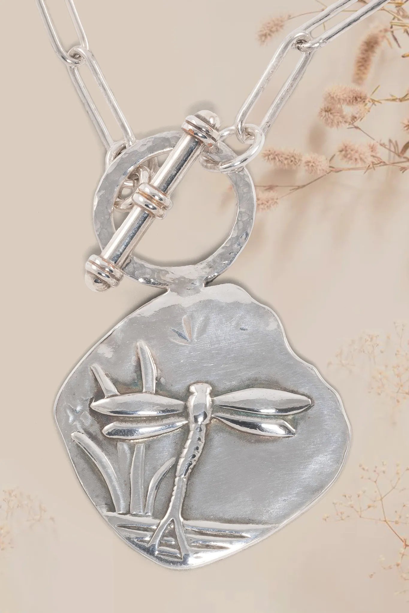 Silver necklace with a dragonfly pendant on a beige background