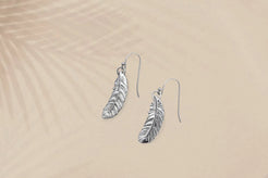 Silver feather-shaped earrings on a beige background