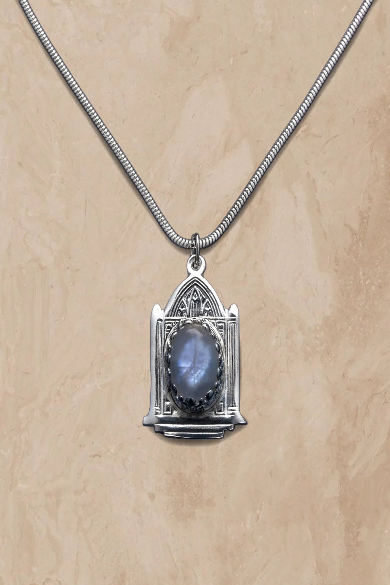 Silver necklace with a pendant featuring a blue stone on a beige background