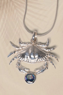 Silver crab pendant with a colorful gemstone on a beige background