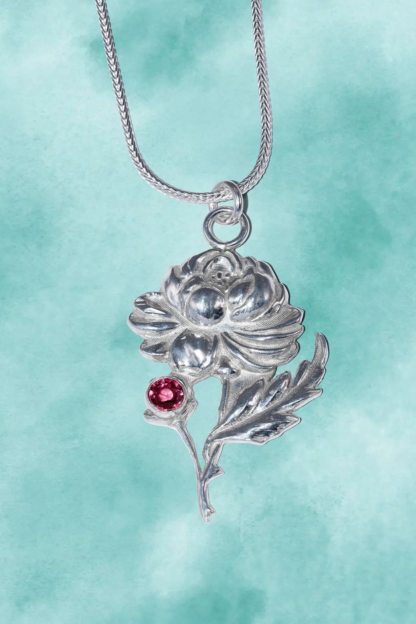 Silver flower-shaped pendant with a red gemstone on a light blue background