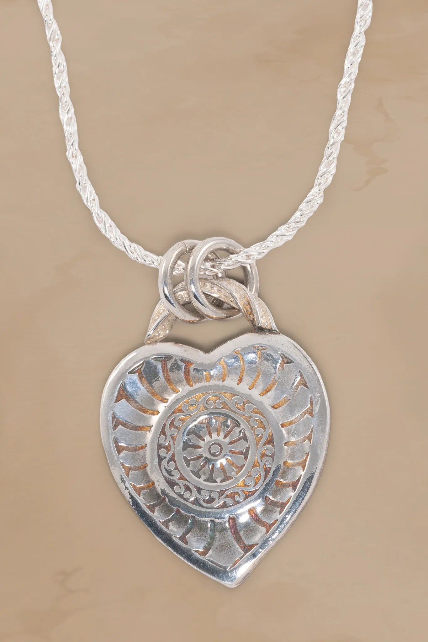 Silver heart-shaped pendant with intricate design on a beige background