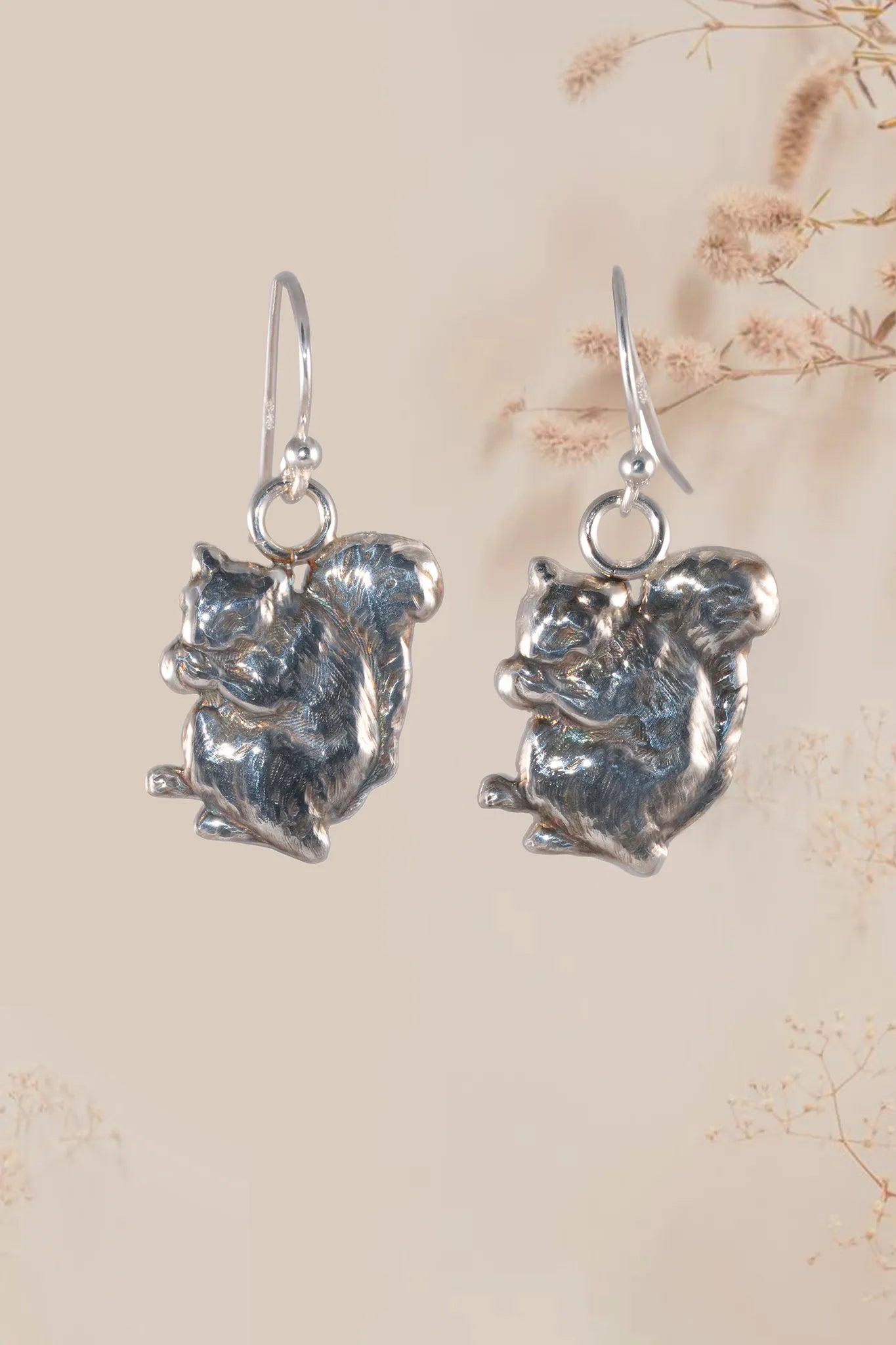 Silver squirrel-shaped earrings on a beige background with floral patterns