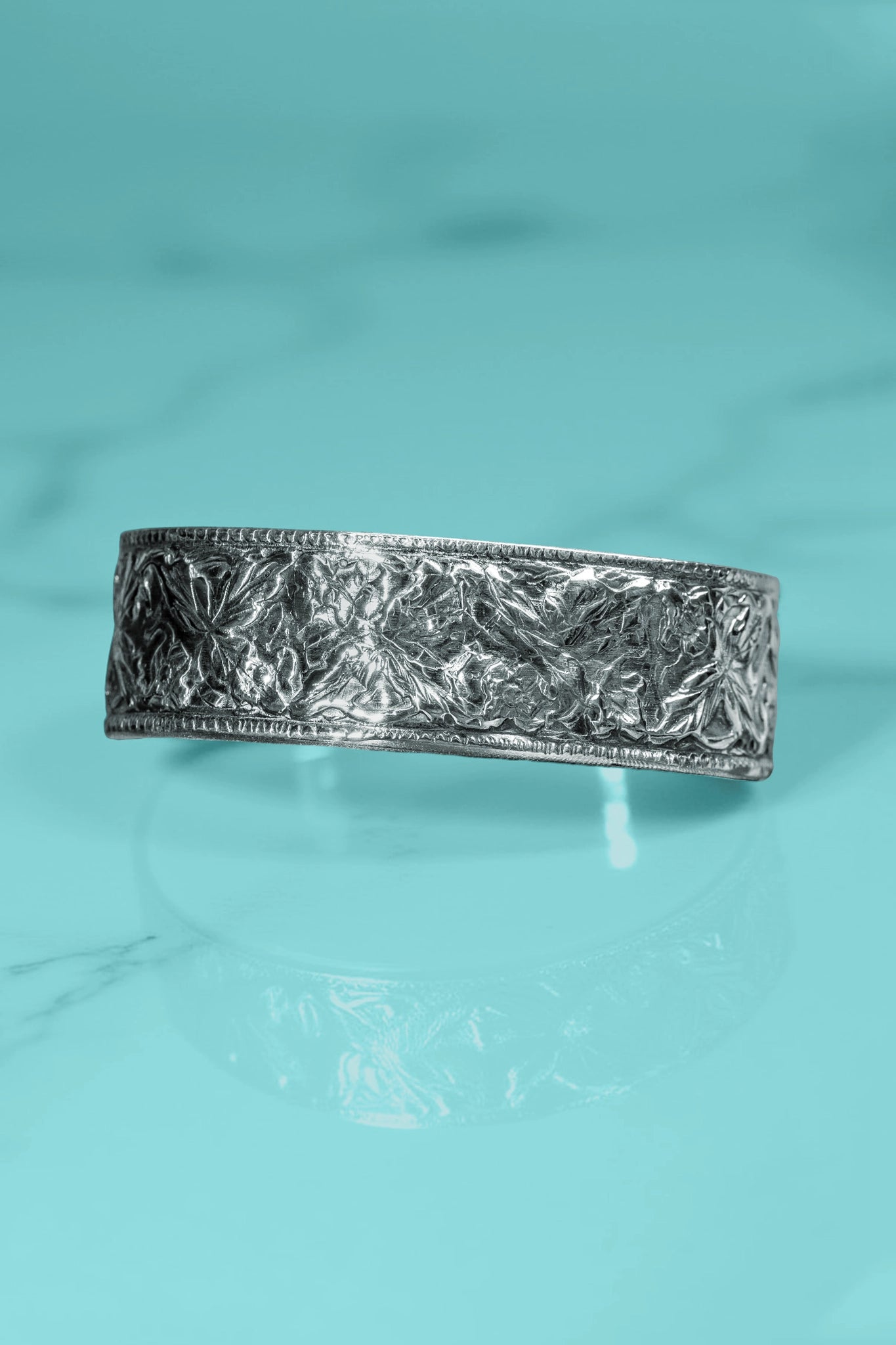Silver bracelet with textured design on a turquoise background