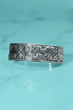 Silver bracelet with textured design on a turquoise background